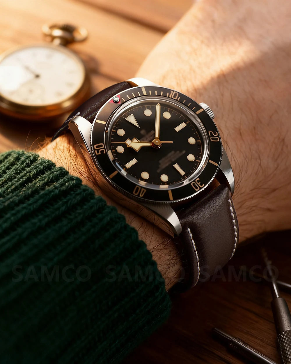 A close-up of a brown leather watch with quick release pins on a wrist, next to a vintage pocket watch.