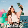A woman is holding a green silicone earphone case with a strap outdoors against a blue sea background.
