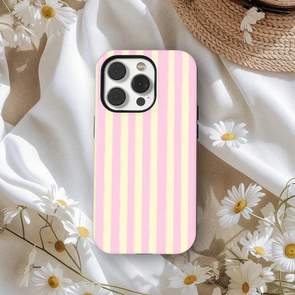 A pink and yellow striped magnetic dual-layer phone case for an iPhone resting on a white fabric surrounded by white daisies.