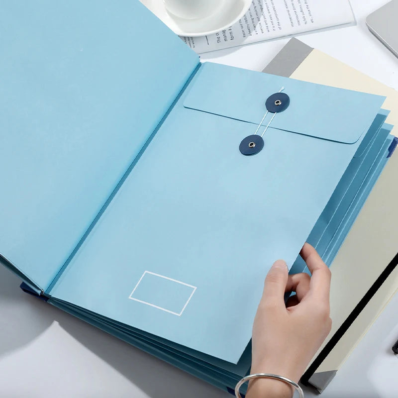 A hand is opening a light blue expanding accordion document organizer file folder on a white surface.