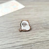Un pequeño broche de esmalte redondo que representa la cara de un gato blanco lindo con acentos marrones.