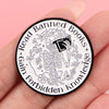 A black enamel lapel pin featuring a detailed illustration of a skeleton surrounded by books and text.