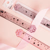 A plastic ruler marked with cat paw prints is shown next to a pink ribbon and a small product label.