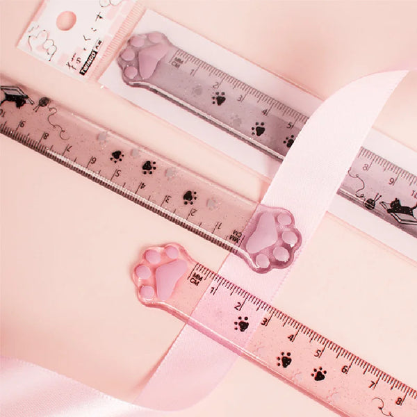 A plastic ruler marked with cat paw prints is shown next to a pink ribbon and a small product label.