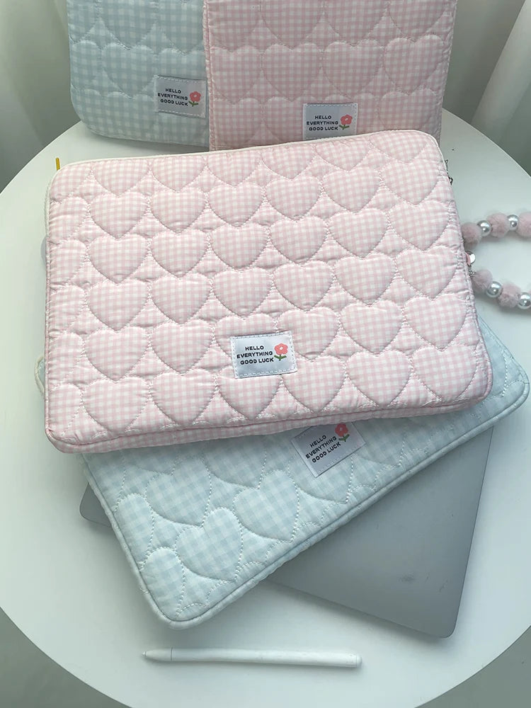 A stack of pink and light blue quilted laptop sleeves with a hello everything good luck tag.