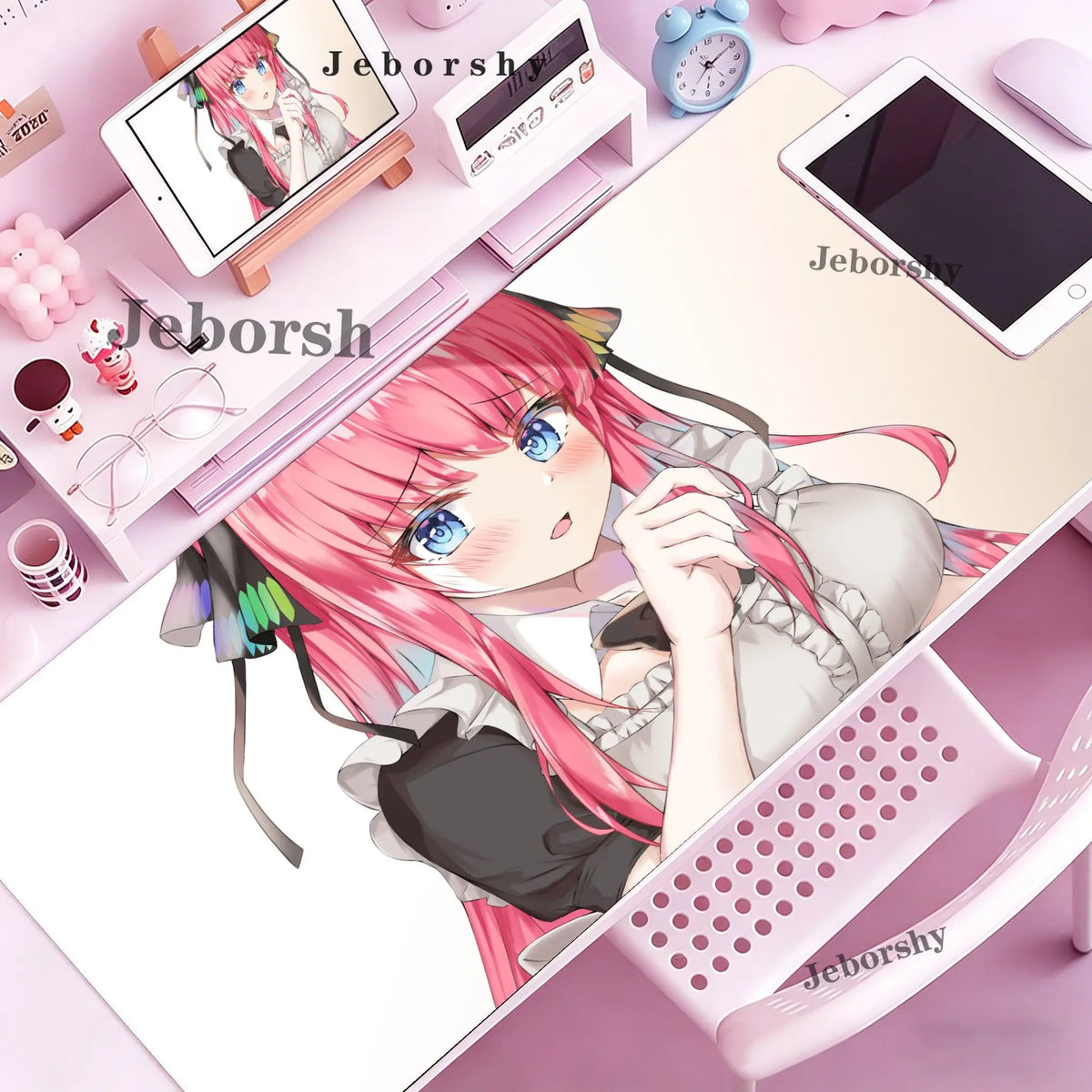 A close-up of a pink-haired anime girl relaxing on a pink desk mat with various stationery items and a tablet.