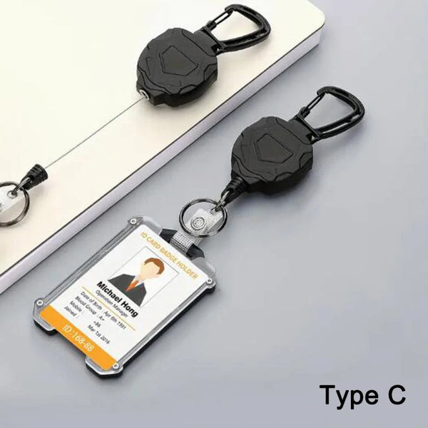 A black retractable badge clip with a clear ID card holder is shown on a white surface.