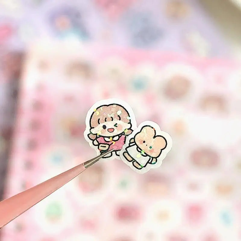 A hand is applying a cute cartoon sticker featuring a smiling, fluffy character to a sheet of patterned paper.