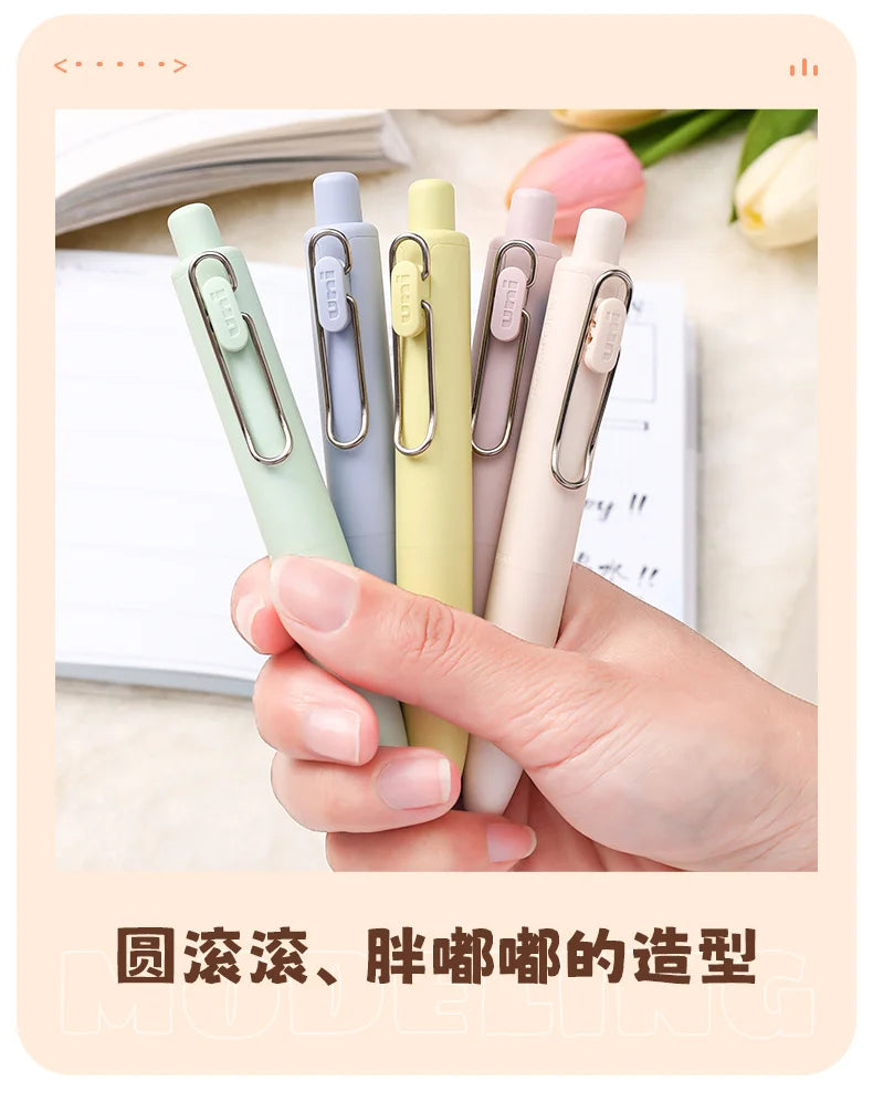 A hand holds several pastel colored Uni-Ball One Mini Cute Gel Pens, showcasing their compact design and smooth finish.