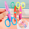 Una mano sostiene unas tijeras de manualidades rosas junto a un juego de seis tijeras coloridas, incluyendo verdes, amarillas