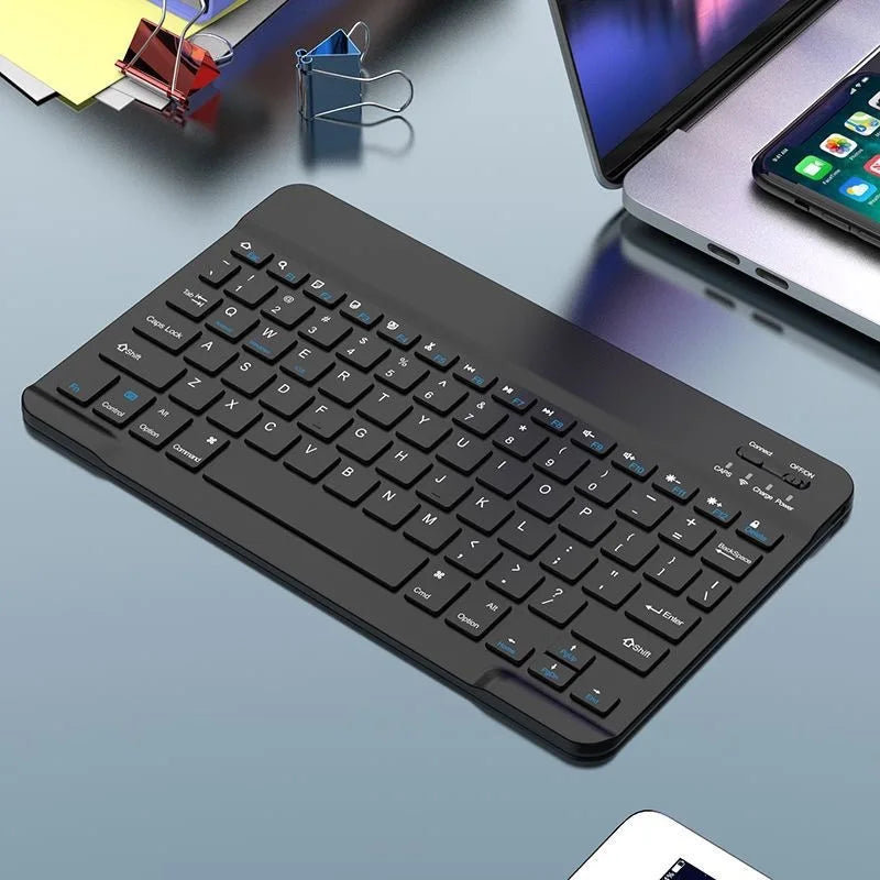 Schwarzes Mini-Bluetooth-Tastatur- und Maus-Set neben einem Tablet auf grauer Oberfläche.