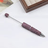 A silver pen accessory featuring a purple rhinestone bead on the tip and a textured body.