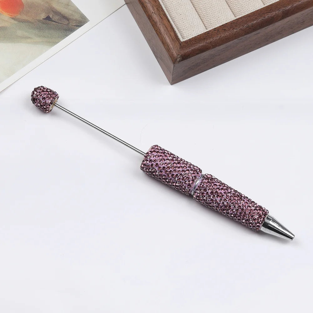 A silver pen accessory featuring a purple rhinestone bead on the tip and a textured body.