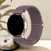 A close-up of a mauve woven nylon watch strap with a rose gold buckle and a black smartwatch face resting on a light surface.