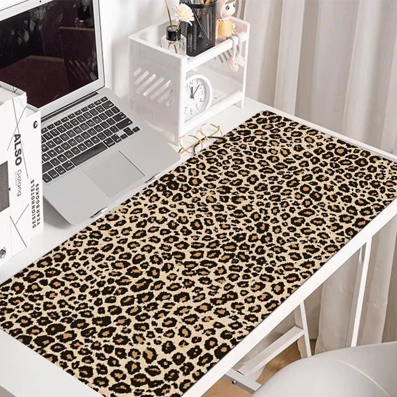 A leopard print XXL gaming mouse pad placed on a white desk next to a laptop and decorative items.