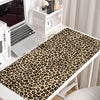A leopard print XXL gaming mouse pad placed on a white desk next to a laptop and decorative items.