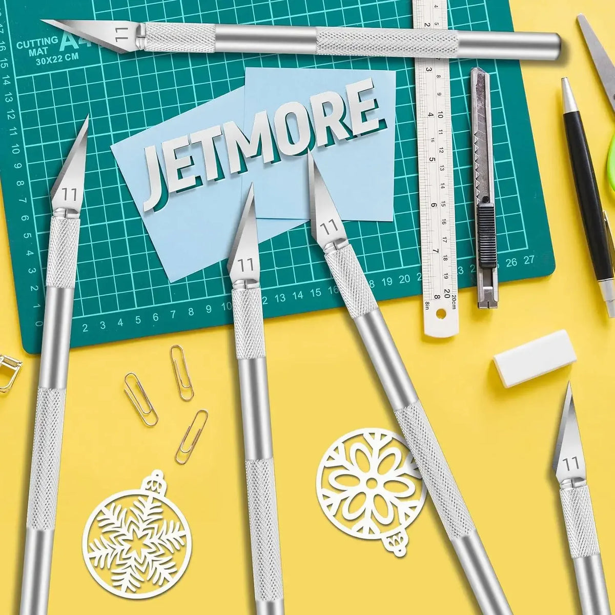 A collection of silver precision craft knives and blades laid out on a green cutting mat with various tools.
