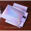 A stack of iridescent rainbow foil bubble mailers for gifts and documents resting on a wooden surface.
