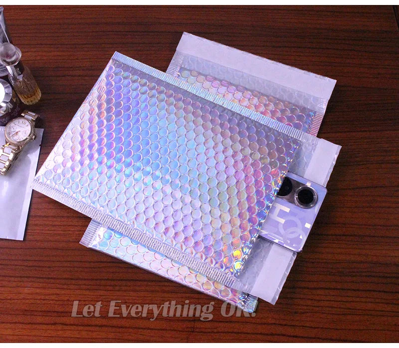 A stack of iridescent rainbow foil bubble mailers for gifts and documents resting on a wooden surface.