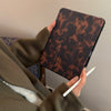 Eine Person hält eine braune Leopardenmuster-Lederhülle für ein iPad und schreibt darauf mit einem weißen Stift.