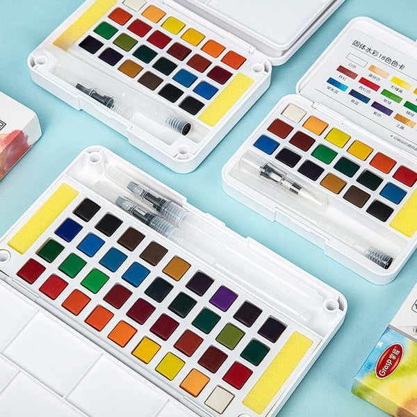 Un set de peinture aquarelle ouvert montrant diverses couleurs et des pinceaux à encre d'eau, disposés de manière organisée.