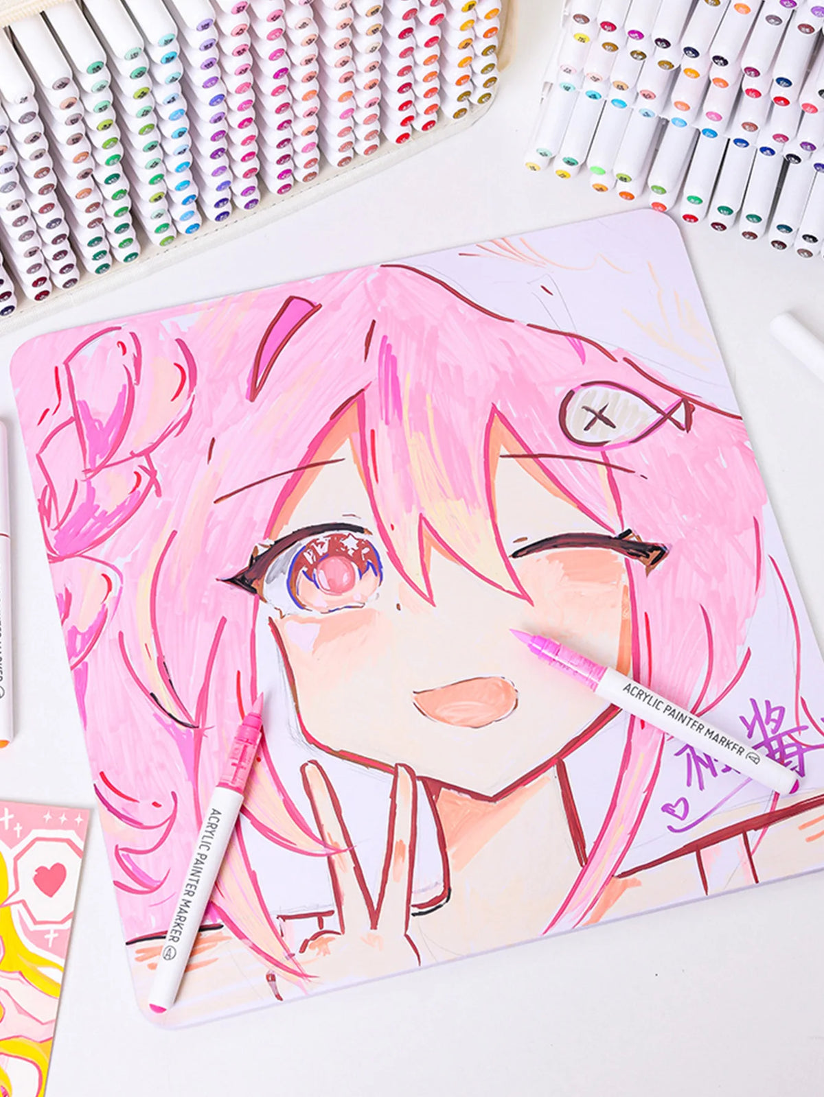 A close-up of a hand-drawn illustration featuring a pink-haired anime character, surrounded by acrylic paint markers.