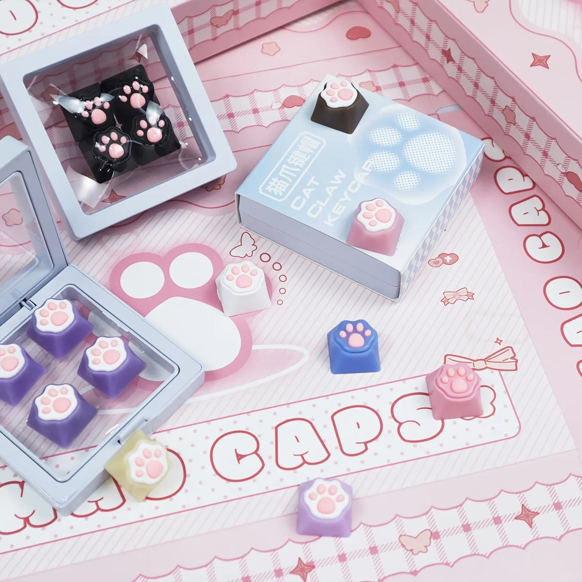 A collection of pink and purple cat paw keycaps and heart keycaps displayed in packaging on a pink surface.