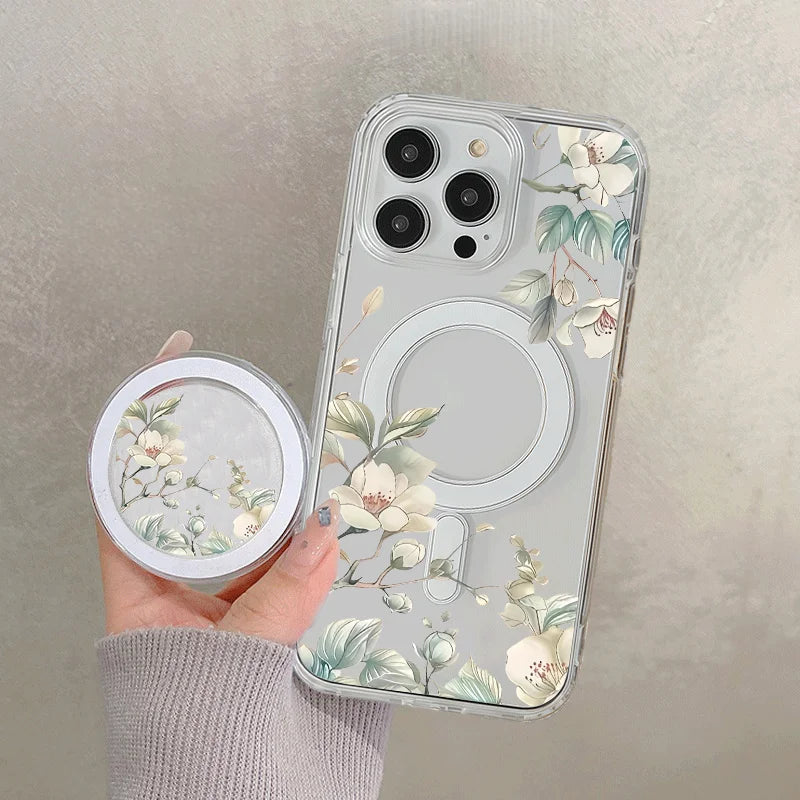 A hand holds a clear floral magnetic phone case for an iPhone featuring white and green botanical designs.