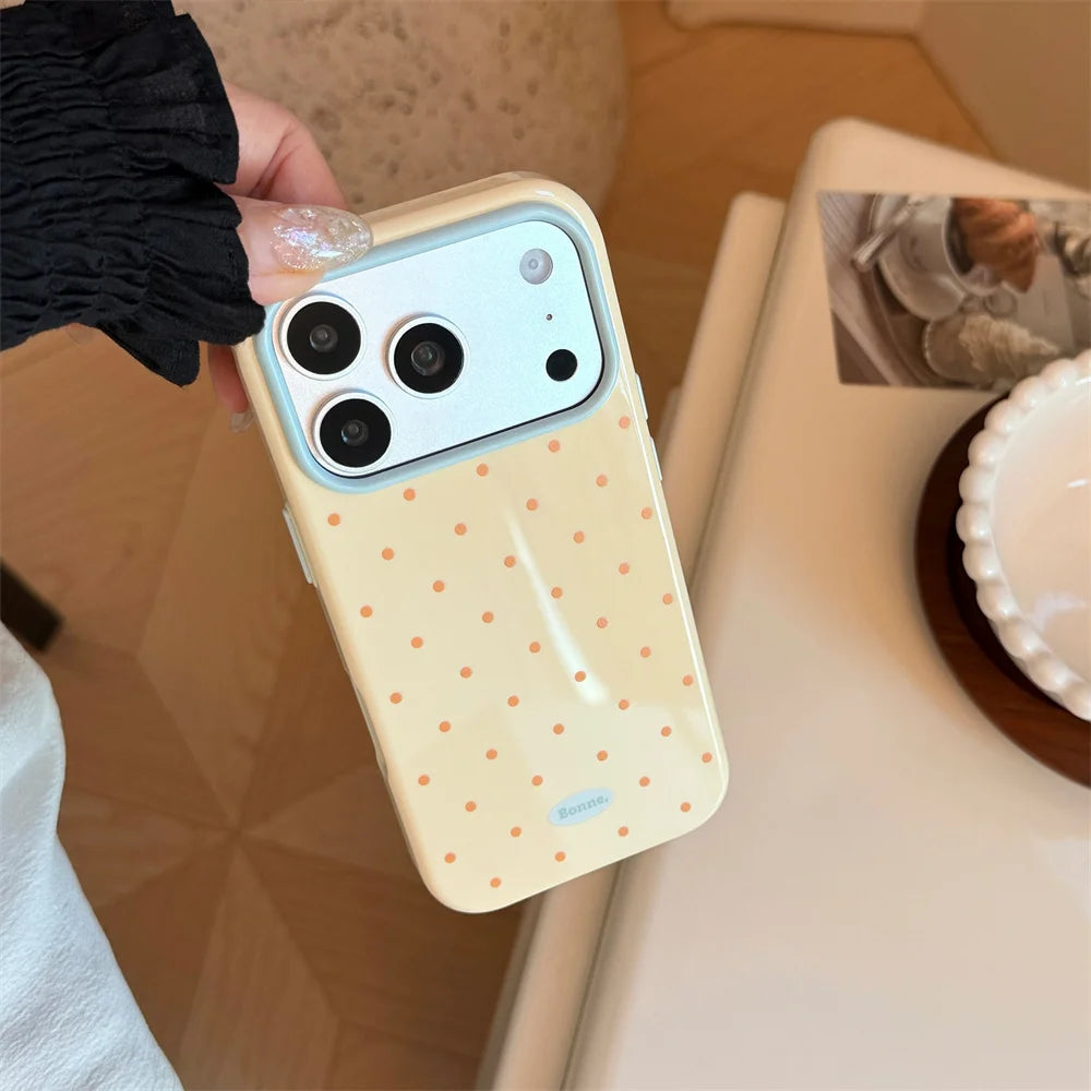 A hand holds a light yellow phone case with orange polka dots and a clear silicone shockproof cover for an iPhone.
