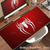 A red desk mat featuring a white spider-man design placed on a wooden desk next to a computer monitor.