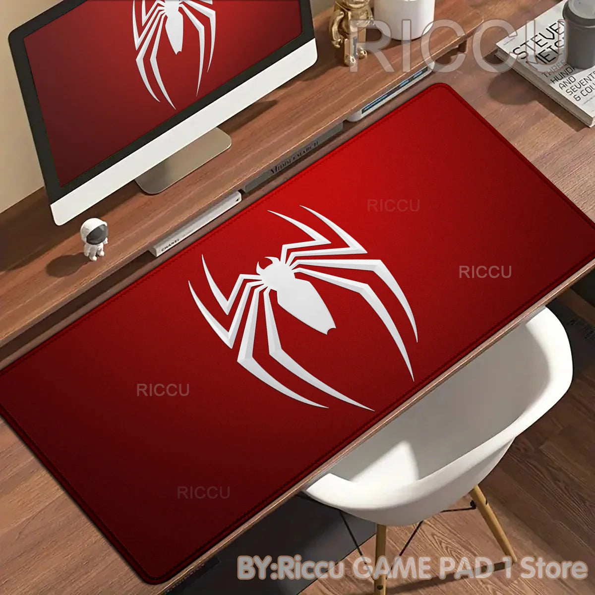 A red desk mat featuring a white spider-man design placed on a wooden desk next to a computer monitor.