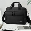 A black Oxford cloth crossbody briefcase with a laptop compartment and shoulder strap resting on a white surface.