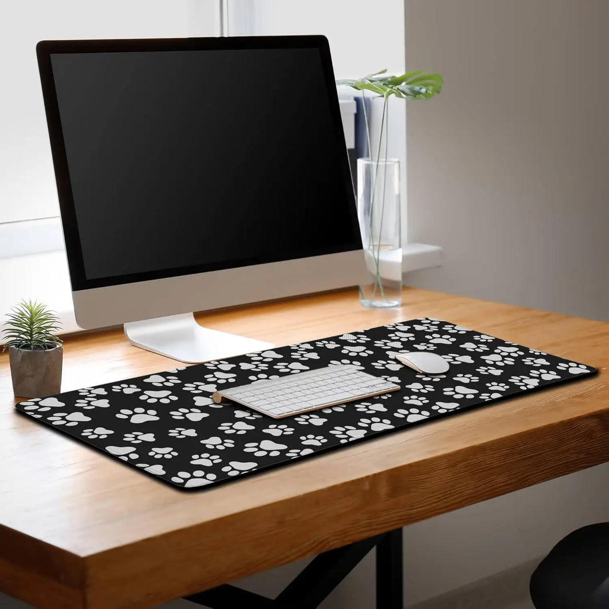 Black pet paw print desk mat placed on a wooden desk in an office setting.