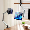 An adjustable aluminum tablet stand holds a tablet and two smartphones on an arm, positioned near a window.
