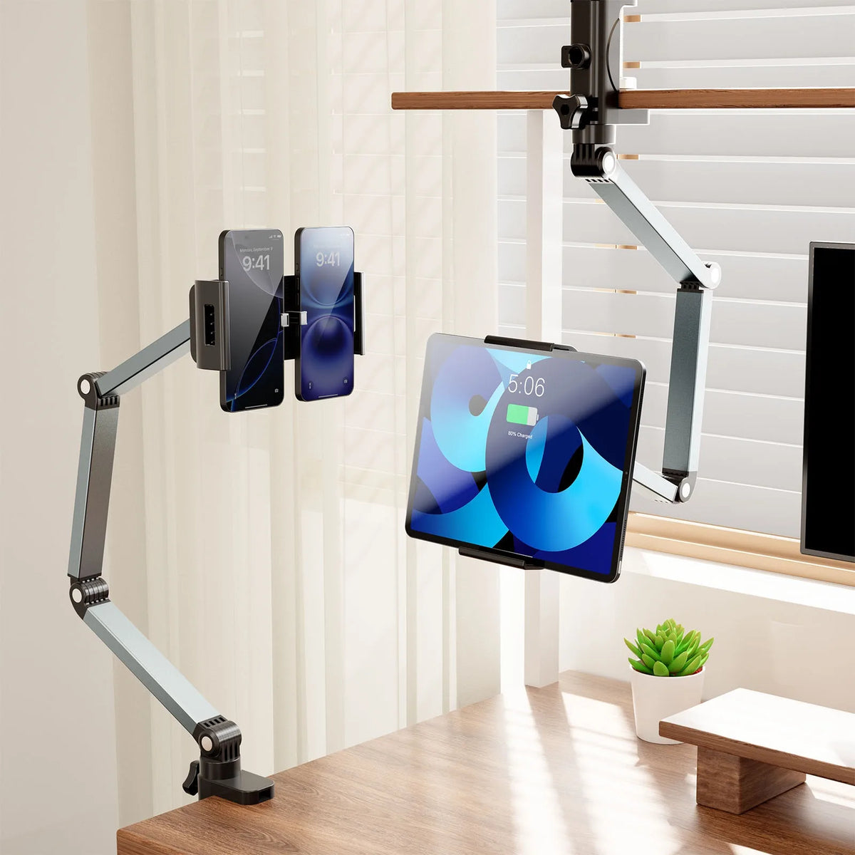 An adjustable aluminum tablet stand holds a tablet and two smartphones on an arm, positioned near a window.