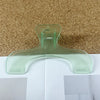 A clear, translucent book page clip is shown resting on a white surface against a textured brown background.