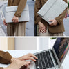 Eine Frau hält eine hellgraue Premium-Leder-Laptophülle und einen braunen Blazer, mit einem geöffneten Laptop auf einer weiße