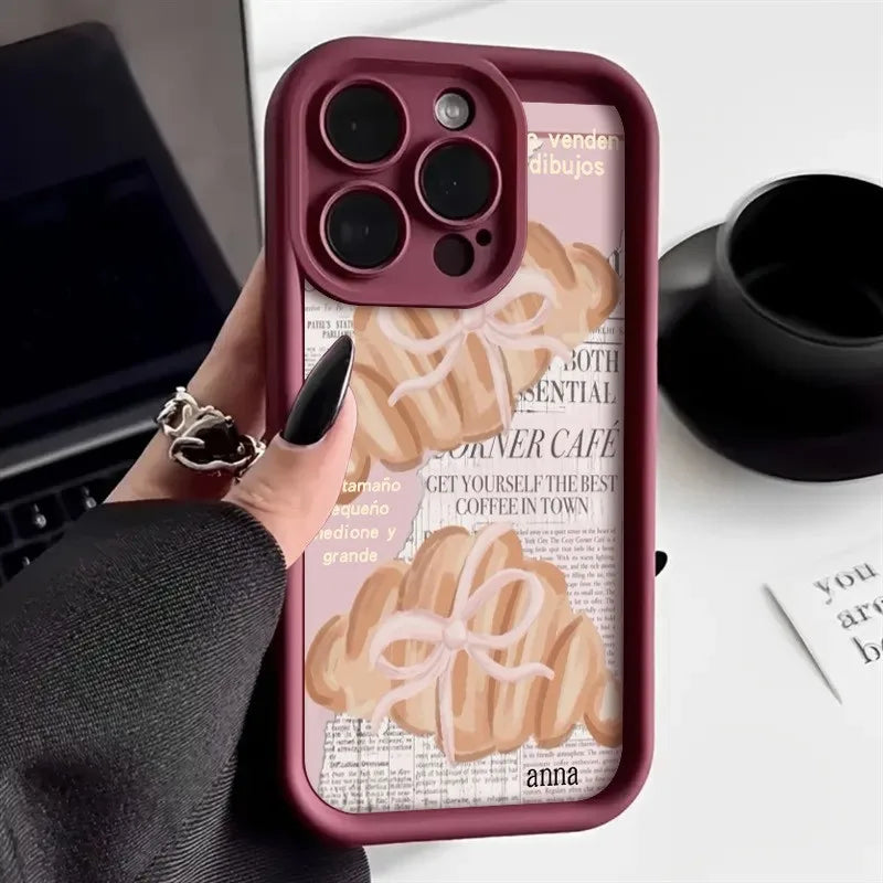 A close-up of a pink phone case with a croissant newspaper pattern featuring the name anna.