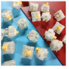 A collection of milky yellow pro hotswap mechanical keyboard switches arranged on a red and blue surface.