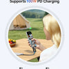 A woman is using a device that supports 100W PD charging to charge a smartphone outdoors.