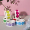 Rolls of round dot labels in various colors including yellow, pink, purple, and blue on a white background