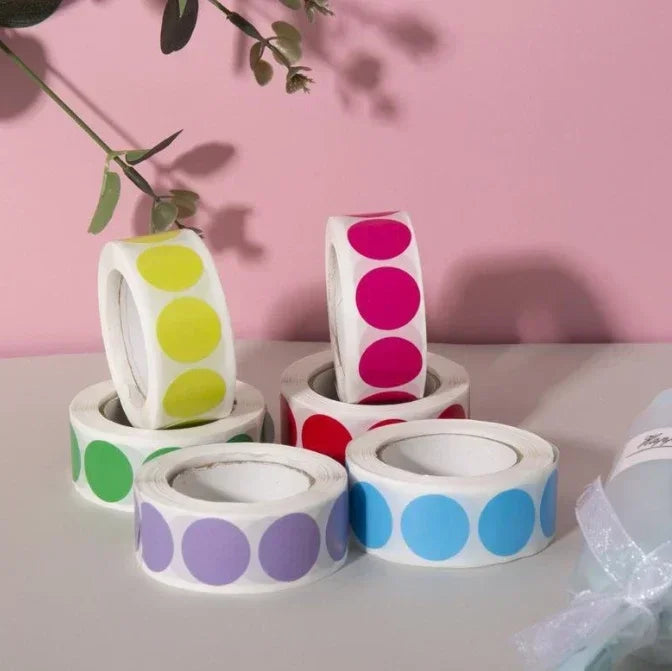 Rolls of round dot labels in various colors including yellow, pink, purple, and blue on a white background