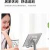 A woman is using a foldable desktop phone stand on a wooden table for casual use.