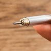 A close-up shot of a metal pencil tip being held by a finger, showing the precision mechanical pencil set.