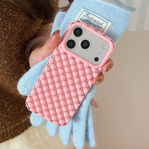 A pink 3D pearl hollowed phone case for an iPhone is being held by a person wearing light blue knitted gloves.
