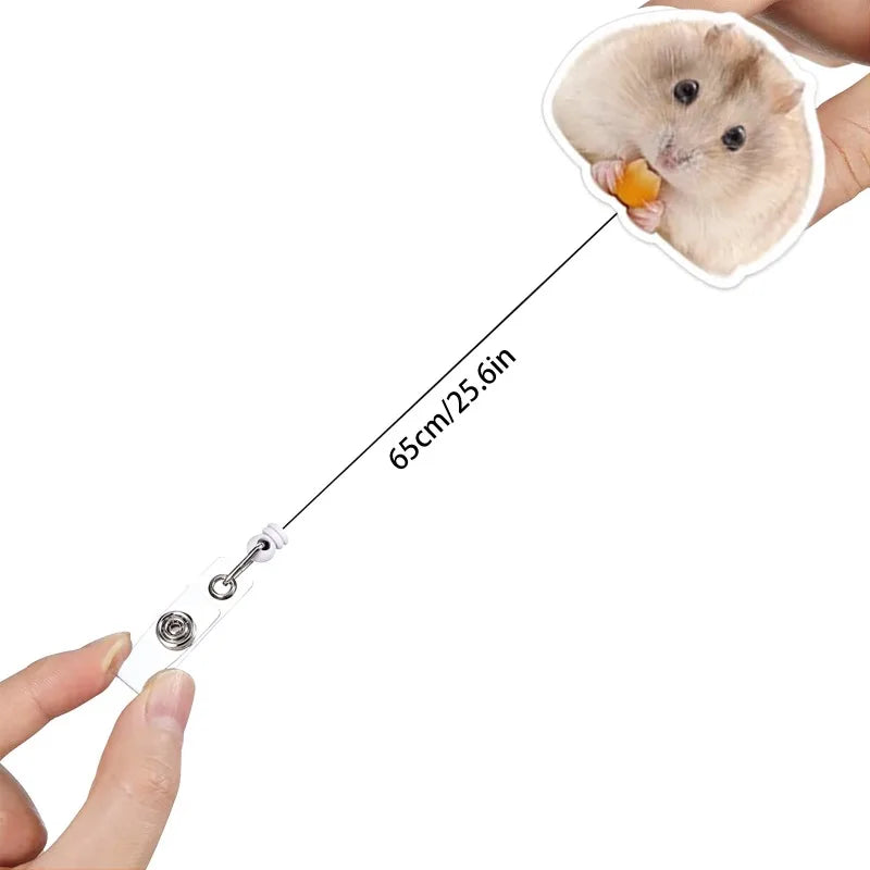 A hand is attaching a acrylic badge reel to a hamster, showing the size of the clip.