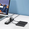 A black USB 3.0 hub extender with multiple cables and power adapters lying on a white desk next to a laptop.