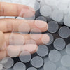 A hand is applying self-adhesive hook and loop fasteners onto a dark surface.