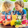 Children holding fruit-shaped sticky notes and fresh fruit on a wooden surface