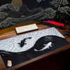 A black and white koi pattern mouse pad featuring a dynamic wave design with fish silhouettes on a wooden desk.